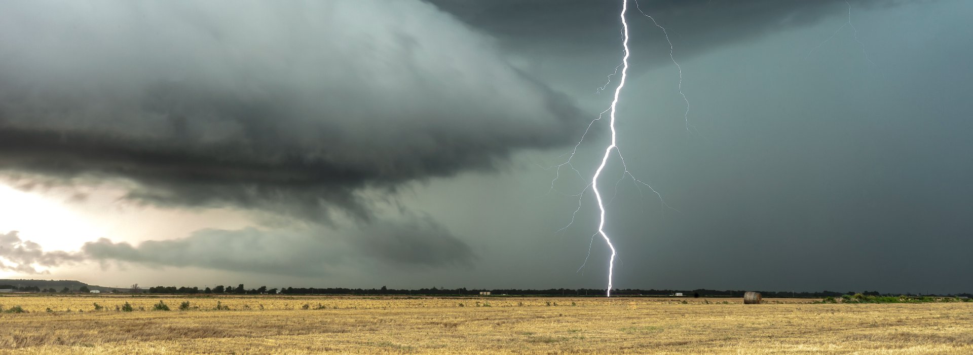 Ein Gewitter auf freiem Feld, ein Blitz schlägt ein, im Hintergrund Wald