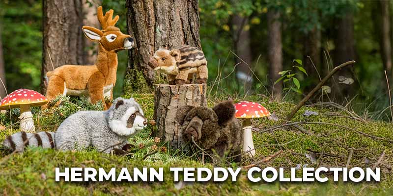 Mehrere Plüschtiere – darunter ein Rehkitz, ein Dachs, ein Waschbär und ein Eichhörnchen – sind in einer Waldszene zwischen Moos, Baumstümpfen und Fliegenpilzen arrangiert; unten steht der Schriftzug ‚Hermann Teddy Collection‘.