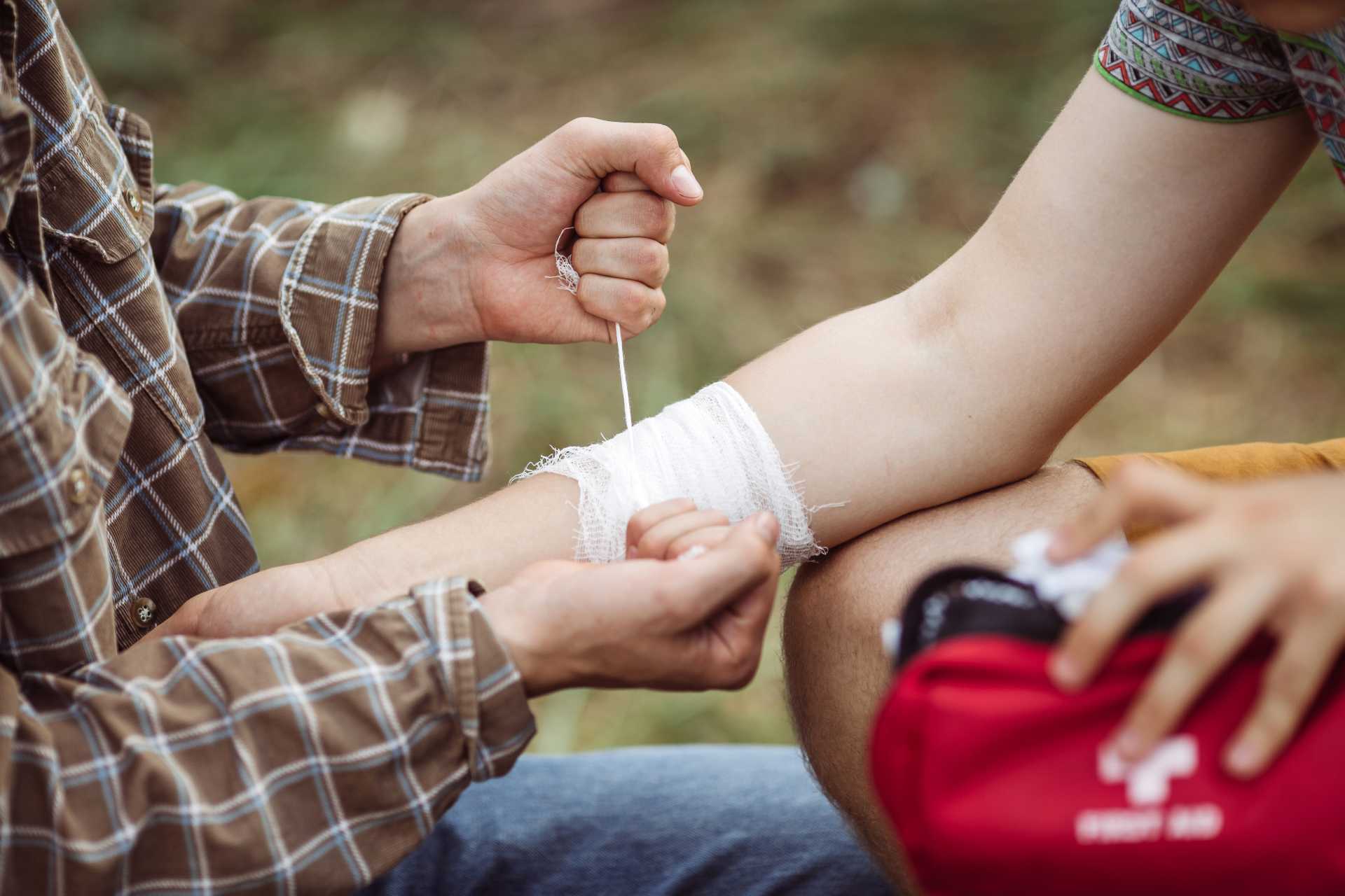 Eine Person leistet outdoor erste Hilfe, verbindet den Arm einer anderen Person